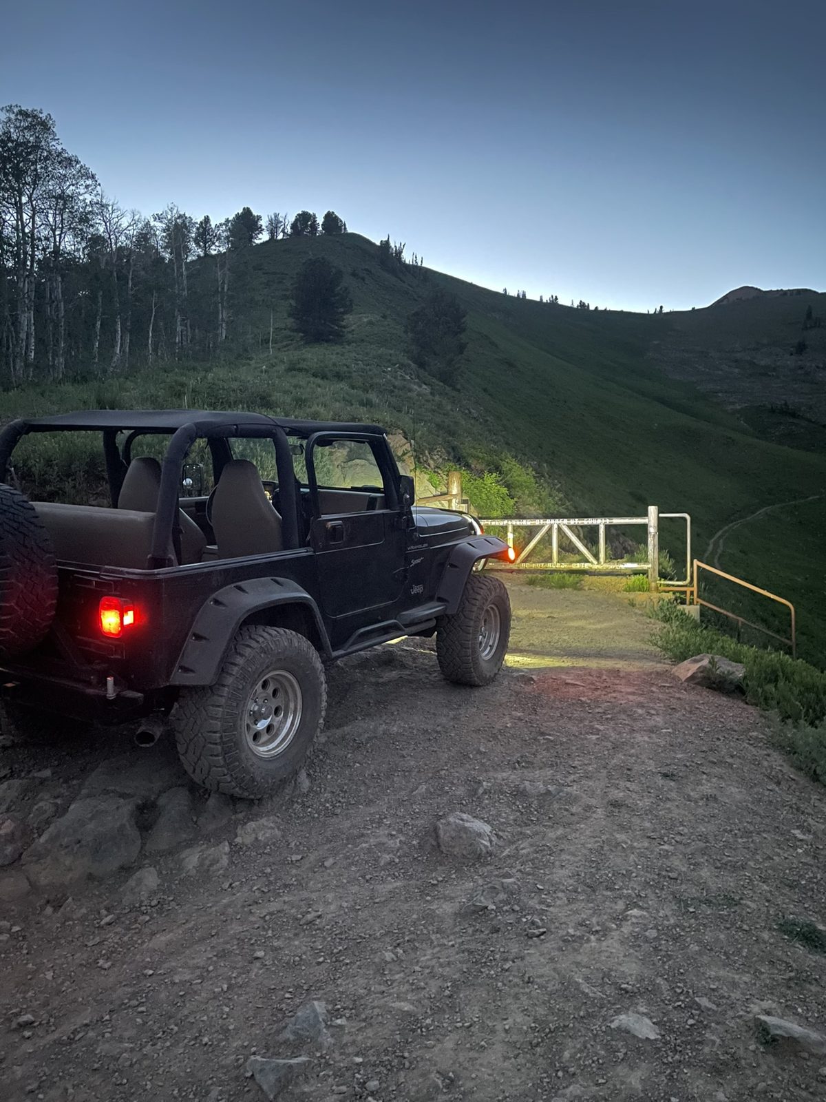 Black Jeep Wrangler parked at a trail gate at dusk in the Utah mountains