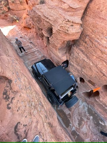 Jeep working its way through a narrow red rock slot canyon