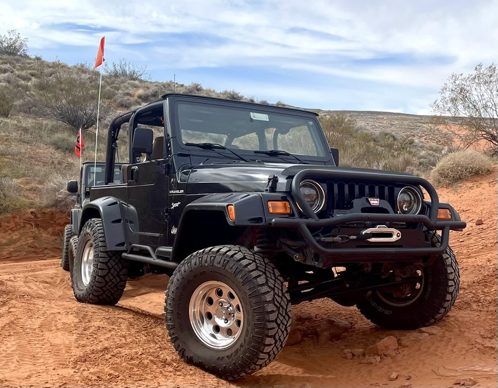 Black Jeep Wrangler with winch bumper on red desert sand